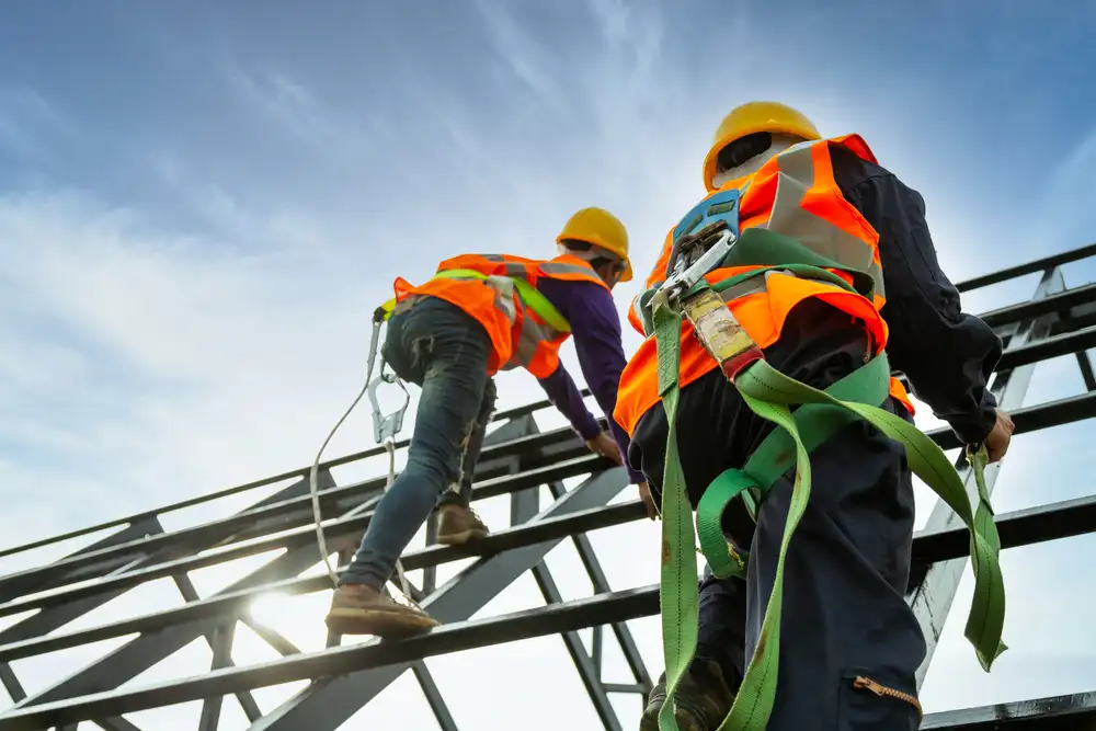 A construction worker wearing a full safety body harness with fall arrestor hooks, secured while working on a high roof structure.